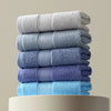 Stack of various thick cotton face and hand towels in shades of gray and blue, showcasing softness and absorbency.