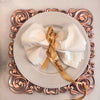 Luxury 12 Inch Eco-Friendly Disposable Round Plate with rolled napkins and ribbon on an ornate charger.
