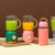 Portable USB Rechargeable Double Cup Juicer with green and yellow smoothies in cups and a pink bottle.