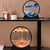 Round 3D Moving Sand Art Frame Hook displayed on a shelf with blue and orange sand designs.