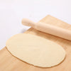 Wooden Rolling Pin next to rolled out dough on a bamboo surface for baking purposes.