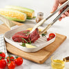 Using Heat Resistant Silicone Tipped Stainless Steel Tongs to handle meat on a cutting board with fresh vegetables.