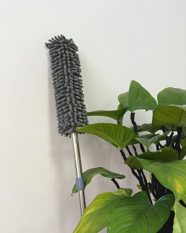 Telescopic Microfiber Removable Duster leaning next to green leafy plant against a white wall.