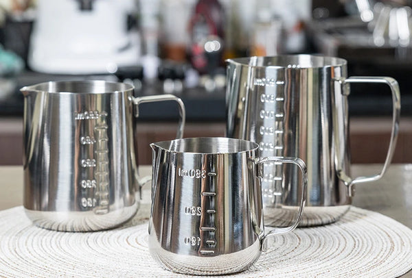 Silver Coffee Latte and Milk Frothing Pitcher 350ML displayed with other milk frothing pitchers on a kitchen counter.