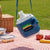 Large Capacity Leakproof Sports Water Bottle hanging in a picnic setting with food containers.