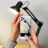 A person holding a smartphone capturing an image of a Flexible Adjustable Swing Arm Clip Desk Lamp.