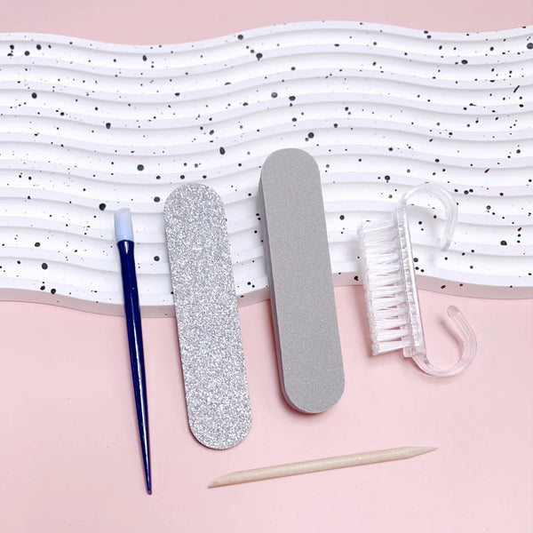 Portable Manicure 6-piece Set tools including files, brushes, and cuticle stick on a pink background.
