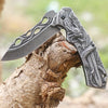 3D Embossed Dragon Folding Survival Knife resting on a tree log, showcasing its intricate design and sharp blade.