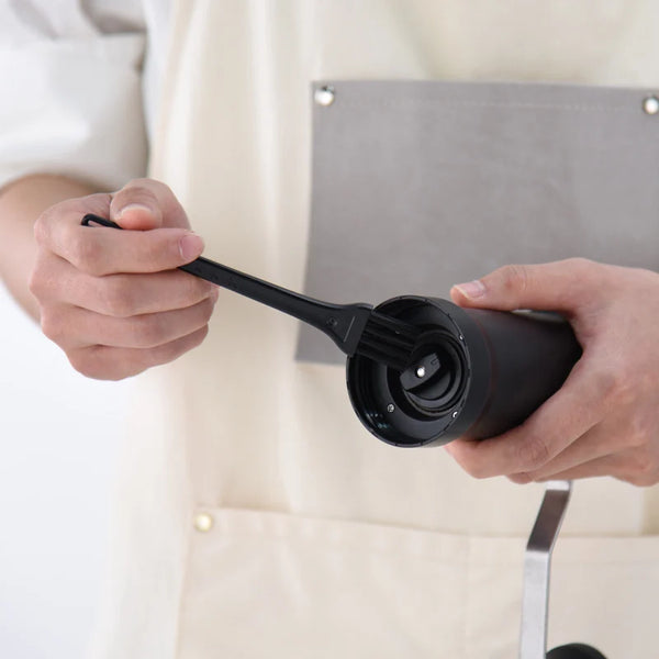 Manual Ceramic Coffee Grinder being cleaned with a brush for optimal maintenance and flavor preservation.
