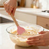 Person using a Silicone Cooking Spoon with Wooden Handle to mix batter in a glass bowl.