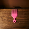 Wide-Tooth Hair Pick Comb in pink color on a wooden surface with a shadow.