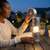 A woman using the Multifunctional Portable Camping Spotlight Flashlight on a table outdoors at night.