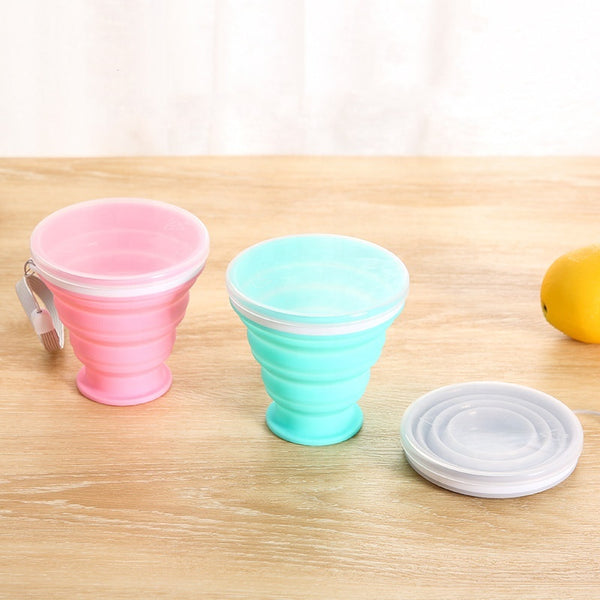 Portable Collapsible Silicone Travel Cup in pink and blue colors on a wooden surface, showcasing their collapsible feature.