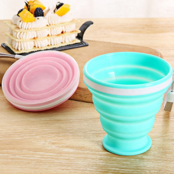 Portable Collapsible Silicone Travel Cup in teal with pink stacked collapsible design on wooden table.