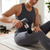 Woman using a Portable Mini Massage Gun on her thigh during home workout.
