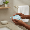 Hands holding the Silicone Care Hair Silicone Scalp Massager in a bathroom setting, showing its texture and design.