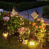Solar-Powered Watering Can Garden Light illuminating a garden with cascading warm lights at dusk.
