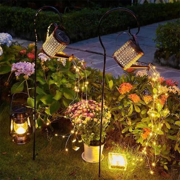 Solar-Powered Watering Can Garden Light illuminating a garden with cascading warm lights at dusk.