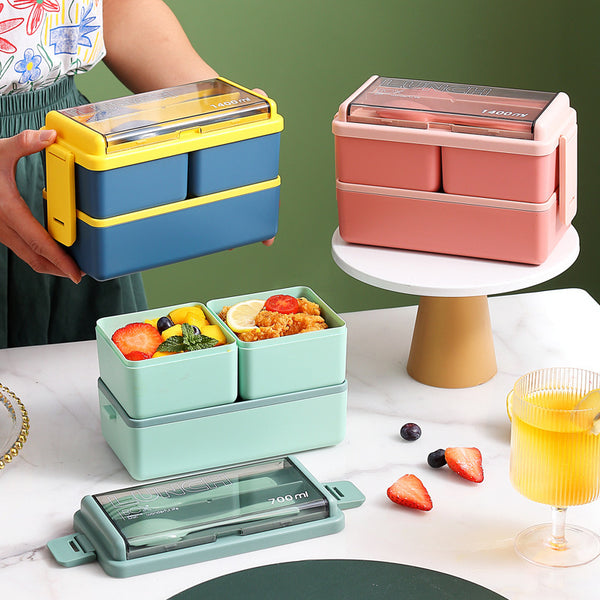 Two-Tier Leakproof Kids Lunch Box in various colors displayed on a table with assorted foods.