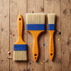 Professional 3 Inch Nylon Paint Brush alongside 1 inch and 2 inch brushes on wooden work surface.