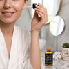 Woman applying Vitamin C Brightening Face Serum with dropper in a bright bathroom setting.