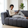 Modern Grey Upholstered 2-Seater Sofa with a woman relaxing and using a tablet in a bright living space.