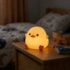 Squishy Silicone Duck Night Light on a wooden table in a cozy bedroom setting.