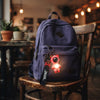 Colorful Astronaut Bear LED Keychain with Wrist Strap attached to a purple backpack, glowing softly in a cafe setting.