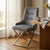 Modern Elegant Upholstered Dining Chair in grey with gold accents, placed beside a wooden table in a bright room.