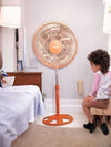 12 Inch Colourful Pedestal Fan standing in a bedroom next to a child sitting on a stool.