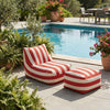 Red and White Striped Outdoor Bean Bag Lounger next to a pool surrounded by greenery and flowers.