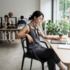 Woman sitting in a Cafe Replica Master Chair, working on a tablet in a modern office environment.
