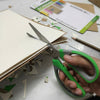 Close-up of Stainless Steel Office Scissors cutting through paper on a desk with craft materials.