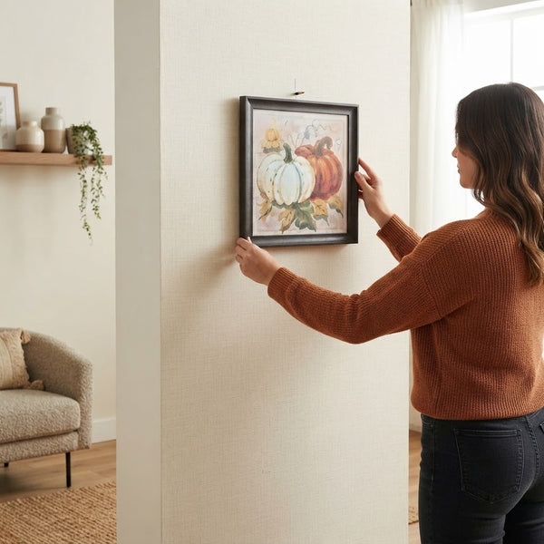 Woman hanging Autumn Pumpkin Framed Wall Art Piece in cozy living room with rustic decor.