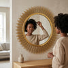A woman admiring herself in the Sunburst Decorative Round Wall Mirror with a stylish gold frame.
