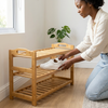 Person organizing shoes on a Standing Bamboo Shoe Rack 3-Tier Organizer in a bright room with plants.