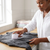 Woman using a Rechargeable Lint Shaver & Fabric Defuzzer on a gray sweater to remove lint and keep fabrics fresh.