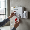 Person activating the 86db Wireless Security Alarm System mounted on a wall with sensors and remote controls.