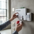 Person activating the 86db Wireless Security Alarm System mounted on a wall with sensors and remote controls.