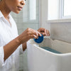 Person adding Solid Blue Disposable Bubble Toilet Cleaner to the toilet tank for easy bathroom cleaning.
