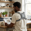Man reading a newspaper while wearing a Spine Posture Corrector and Back Support in a home kitchen.