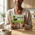 Pure Antioxidant Green Tea packaging held by a person with a cup of tea on the table.