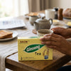 Herbal Tea Ginseng packaging on a wooden table with breakfast items, showcasing natural energy and vitality blend.
