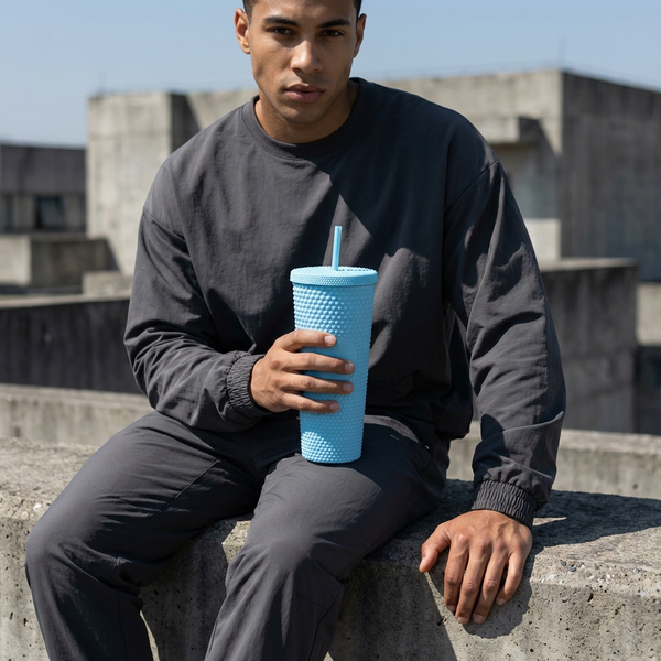 Person holding a Solid Color Plastic Tumbler With Straw while sitting on a concrete ledge outdoors.