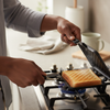 A person using a Double-Sided Aluminum Toast Maker on a gas stove to prepare perfectly toasted bread.