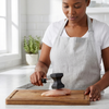 Person using a meat hammer kitchen tenderiser tool to flatten chicken breast on a wooden cutting board.