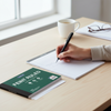 A6 Feint Ruled Duplicate Book Pack placed on a desk, with a person writing notes using a pen.