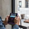 Person holding the R36xx Handheld Game Console displaying a game on its screen at a café table.