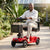 New Model Four Wheel Elderly Mobility Scooter in a garden with a senior man driving it.