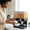 Woman dispensing cereal from a Compact Dry Food Dispenser Dual Control in a modern kitchen.